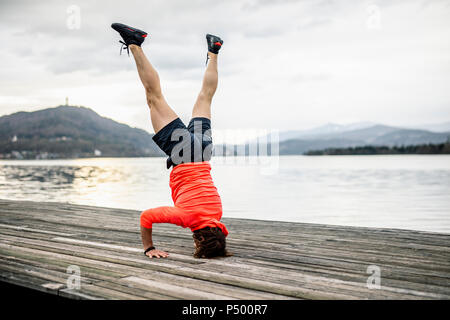 Sportler tun ein Kopfstand auf der Holzterrasse am Seeufer Stockfoto