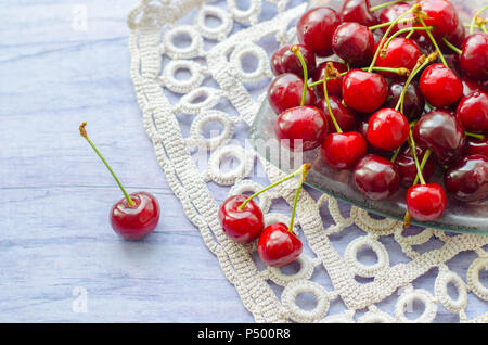 Frische reife Kirschen auf hölzernen Tisch. Kirschen in eine transparente Glasplatte und Küche Serviette. Stockfoto