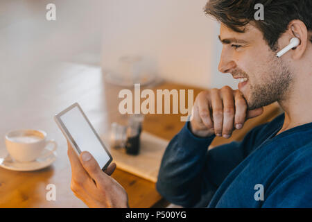 Lächelnd Mann in einem Café mit Ohrhörer mit Tablet Stockfoto