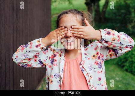 Porträt der lächelnde Mädchen, die Augen mit den Händen Stockfoto