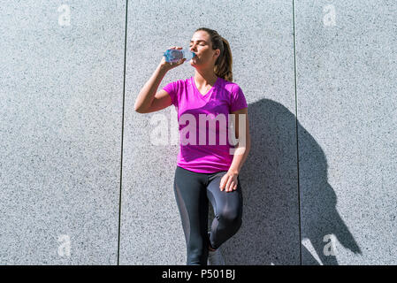 Junge Frau mit einer Unterbrechung von der Ausübung von Trinken aus der Flasche Stockfoto