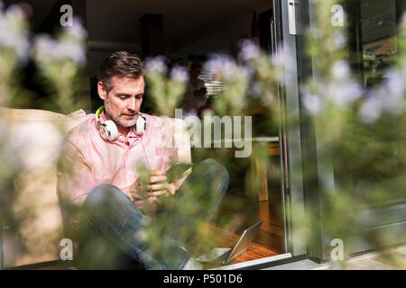 Reifen Mann an der offenen Terrasse Tür sitzen Sie ihr Smartphone Stockfoto