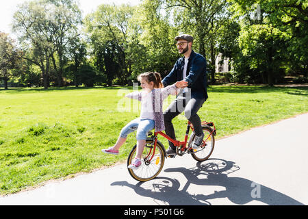 Gerne Vater Reiten Fahrrad mit Tochter in einem Park Stockfoto