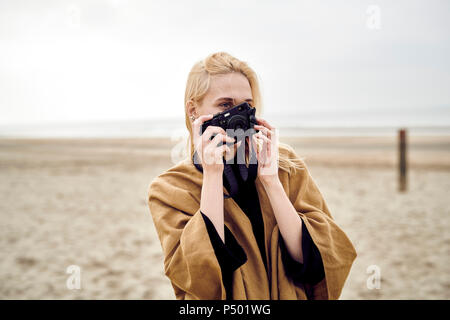 Niederlande, blonde junge Frau nimmt Fotos mit der Kamera am Strand Stockfoto