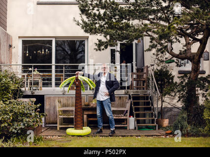 Senior Geschäftsmann steht in seinem Garten, mit einem Gummi Palm, träumen von Urlaub Stockfoto