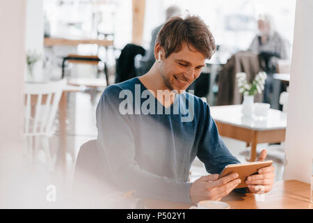 Lächelnd Mann in einem Café mit Ohrhörer mit Tablet Stockfoto