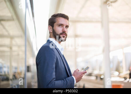Junge Unternehmer holding Handy seitlich auf der Suche Stockfoto