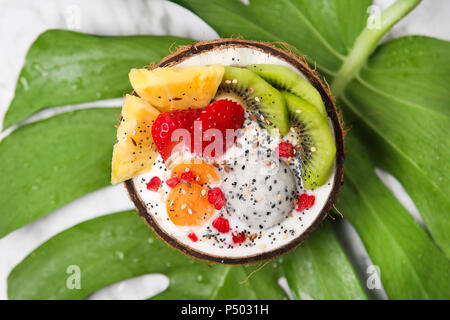 Kokosnuss Schale mit Variuos Früchte, Joghurt und Samen auf Blatt Stockfoto