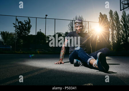 Portrait von tätowierten jungen Mann sitzt auf Basketball bei Sonnenuntergang Stockfoto