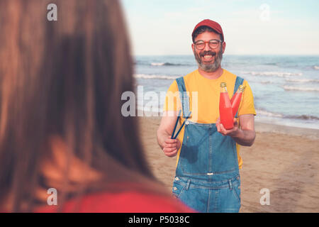 Glückliche Menschen in Latzhosen am Strand bietet Soft drink zu Frau Stockfoto