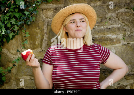 Portrait der junge blonde Frau mit Sonnenhut essen Apple Stockfoto