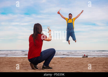 Frau unter Smartphone Bild der glücklichen Mann springen auf den Strand Stockfoto