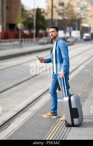 Junger Mann an einer Station mit Smartphone in die Hand und Wagen warten Stockfoto