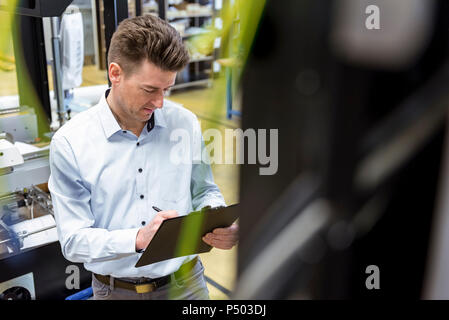 Mann mit Zwischenablage in der Fabrik von Notizen Stockfoto