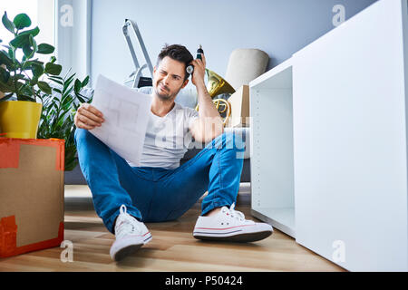 Frustrierter mann Lesen der Anweisungen während der Montage Möbel in der neuen Wohnung Stockfoto
