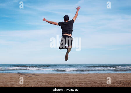 Rückansicht des Menschen springen in die Luft am Strand Stockfoto