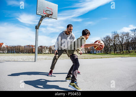 Vater und Sohn spielen Basketball auf Gericht im Freien Stockfoto