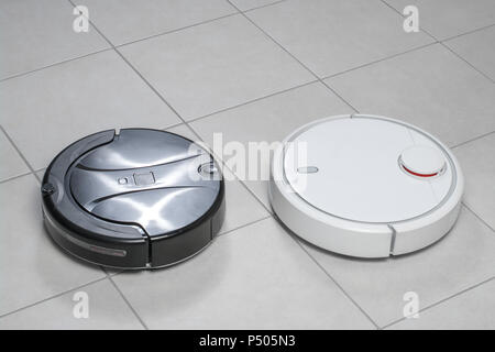 Zwei verschiedene Roboter Staubsauger Modelle Reinigung Staub auf Fliesenboden. Moderne Reinigungstechnik und Sauberkeit. Close Up. Stockfoto