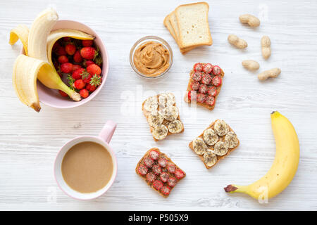 Ansicht von oben gesundes Frühstück: Latte, vegan Toast mit Früchten, Samen, Erdnussbutter. Weiß Holz- Hintergrund. Von oben. Flach. Stockfoto