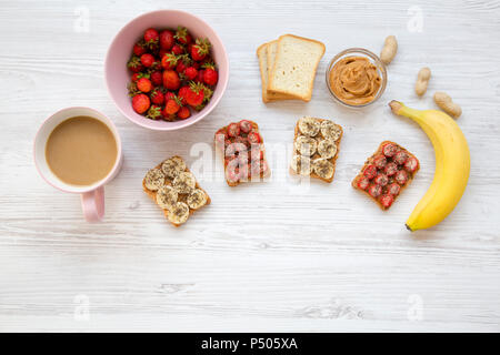 Gesundes Frühstück mit Latte. Vegan Toast mit Früchten, Samen, Erdnussbutter. Weiß Holz- Hintergrund, Ansicht von oben. Von oben. Flach. Stockfoto