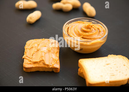 Schüssel mit Erdnussbutter, Toast, ohne schale Erdnüsse auf schwarzen Hintergrund, Seitenansicht. Close-up. Stockfoto