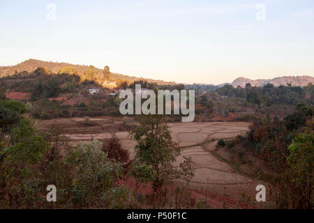 Reisfelder in der trockenen Jahreszeit neben kleines Dorf im ländlichen Myanmar Stockfoto