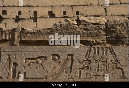 Relief zeigt Gott Amun mit toller Helm mit zwei großen Federn und Bart sitzt auf dem Thron. Ersten Hof des Ramses II. Neuen Imperiums. Tempel von Luxor. Ägypten. Stockfoto