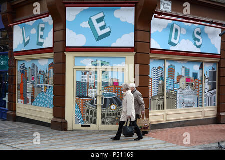Ein älteres Paar Spaziergang, vorbei an einem leeren Storefront mit einem Hintergrundbild Abbildung der Stadt Leeds, Leeds, England, Vereinigtes Königreich. Stockfoto