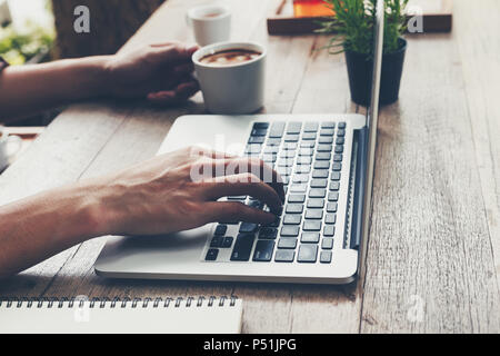Business mann Eingabe Laptop und Holding Kaffeetasse auf Holz Tisch. Stockfoto