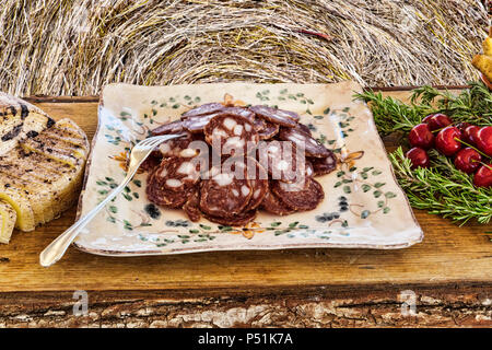 Italienischen Aromen: geschnittene Salami in eine Platte auf einem Holztisch mit Oregano und Kirschen verziert - selektive Fokus Stockfoto