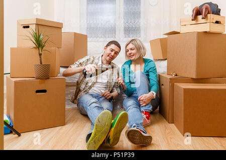 Foto von Mann mit einer Flasche Wein und Frau sitzt auf einem Sofa unter Kartons Stockfoto