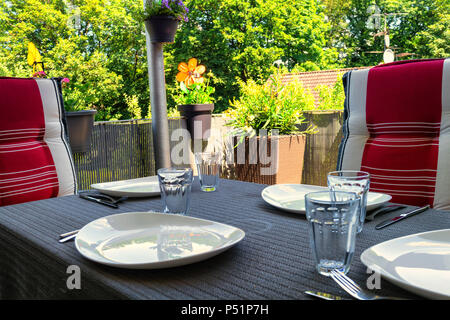 Überdachter Balkon mit Tisch mit weißen Platten, Trinkgläser und Esstisch mit zwei Stühlen mit modernen Sitzbezüge. Stockfoto