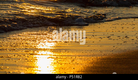 Schöne bunte Formen durch brechende Wellen auf einem Sandstrand und Sonne Reflexionen bei Sonnenuntergang erstellt Stockfoto