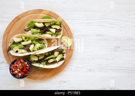 Mais Tortillas mit gegrilltem Rindfleisch, Avocado, Kalk und Salsa auf Holzbrett. Ansicht von oben. Kopieren Sie Raum und Text. Stockfoto