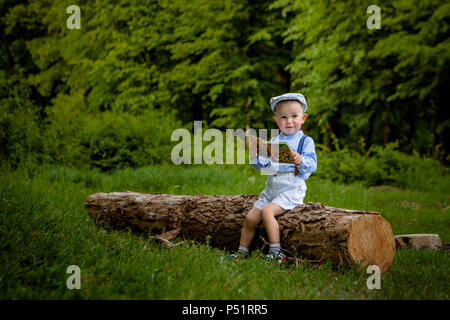 Ein litttle zwei Jahre alte Junge sitzt auf einem Baum und liest ein Buch. hildren Tag. Stockfoto