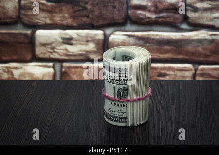 Ein Bündel von Amerikanischen Dollar Wechsel von einhundert Dollar auf einen hölzernen Tisch in der Nähe einer Wand. Stockfoto