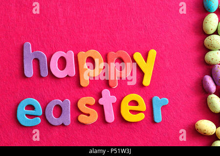 Die Worte frohe Ostern mit Ostern Süßigkeiten gesprenkelten Eier auf einem rosa Hintergrund angezeigt. Stockfoto