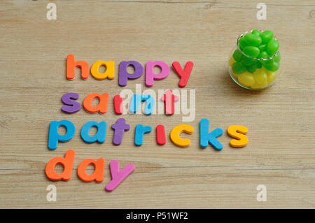Happy Saint Patricks Day in bunte Buchstaben auf einer hölzernen Hintergrund mit einem Topf mit grünen und gelben Jelly Beans gefüllt Stockfoto