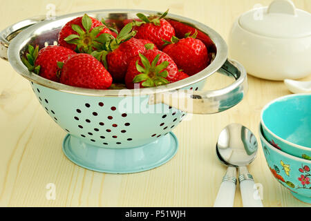 Frisch gepflückt Erdbeeren in Vintage blau Sieb mit Schüsseln und Löffel. Im Querformat und schoss in natürlichem Licht. Stockfoto