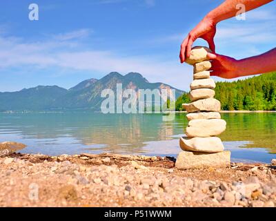 Pyramide von flachen Steinen auf einen Kiesstrand See Strand, die Berge der Spiegelung im glatten Wasser. Stockfoto