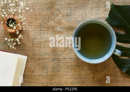 Trinken Sie eine Tasse Tee und ein Buch lesen auf Roh stoff moderne Tisch Szene Stockfoto