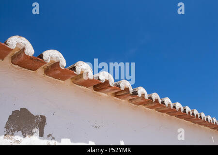 Verwitterte Fassade eines Hauses. Kante eines Daches mit orange Kacheln, erstellen eine diagonale Linie. Strahlend blauen Himmel im Hintergrund. Porches, Algarve, Po Stockfoto