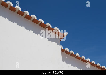 Verwitterte Fassade eines Hauses. Kante eines Daches mit orange Kacheln, erstellen eine diagonale Linie. Strahlend blauen Himmel im Hintergrund. Porches, Algarve, Po Stockfoto