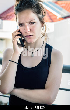 Ein junges Mädchen, das Gespräch per Telefon stehen auf dem Balkon mit schlechten Nachrichten, schockiert. Stockfoto