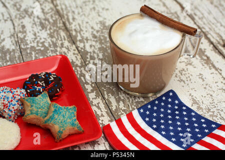 Amerikanische Flagge serviette Kaffee oder einen Cappuccino und Cookies auf einer rustikalen weiß Holz- Hintergrund. Auf dem Glas Becher ist einer Zimtstange sitzt. Stockfoto