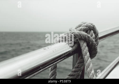 Eine Leine, die an einer Reling eines Bootes befestigt ist, das Wasser im Hintergrund, bei schlechter Sicht. Stockfoto