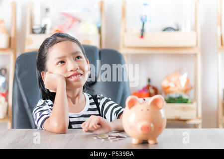 Asiatische Mädchen beim Suchen und Träumen mit sparschwein Metapher Planung für Geld sparen flache Tiefenschärfe wählen Sie Fokus am Schwein Stockfoto