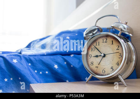 Ein verlassenes Bett mit einem Wecker auf dem Nachttisch. Eine klassische Wecker mit einer leeren Schlafzimmer am Morgen. Stockfoto