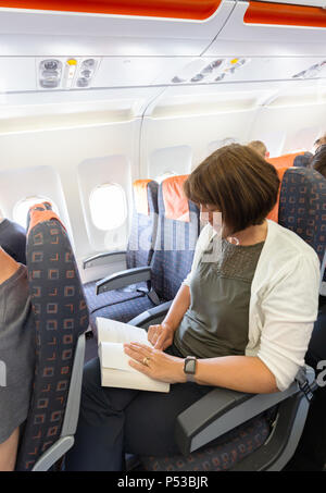 Frau mit einem Buch in einer Ebene, die Kabine während eines Fluges in der economy Sitze, Easyjet Flug Edinburgh nach London, Großbritannien Stockfoto