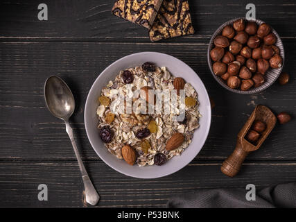 Müsli in Weiß Schüssel auf Grau Schreibtisch mit Nüssen und Keksen rund um. Stockfoto